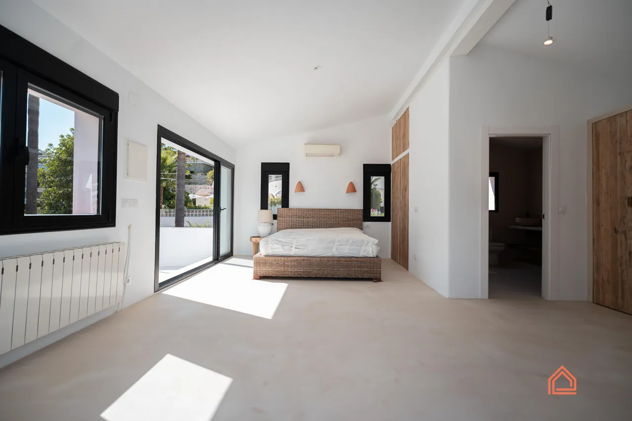 Bedroom with rattan bed, timber doors and sunlit microcement floor