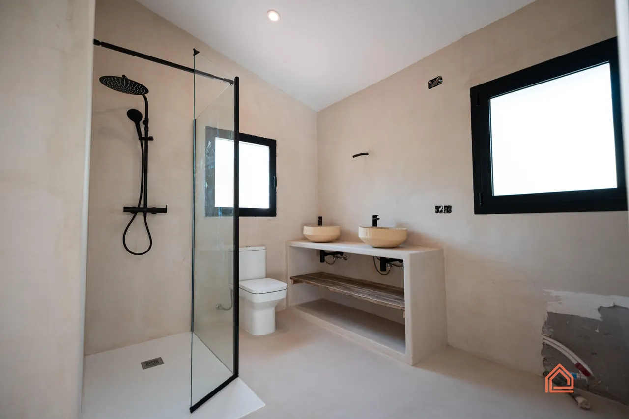 Renovated bathroom with walk-in glass shower, black fittings and microcement walls