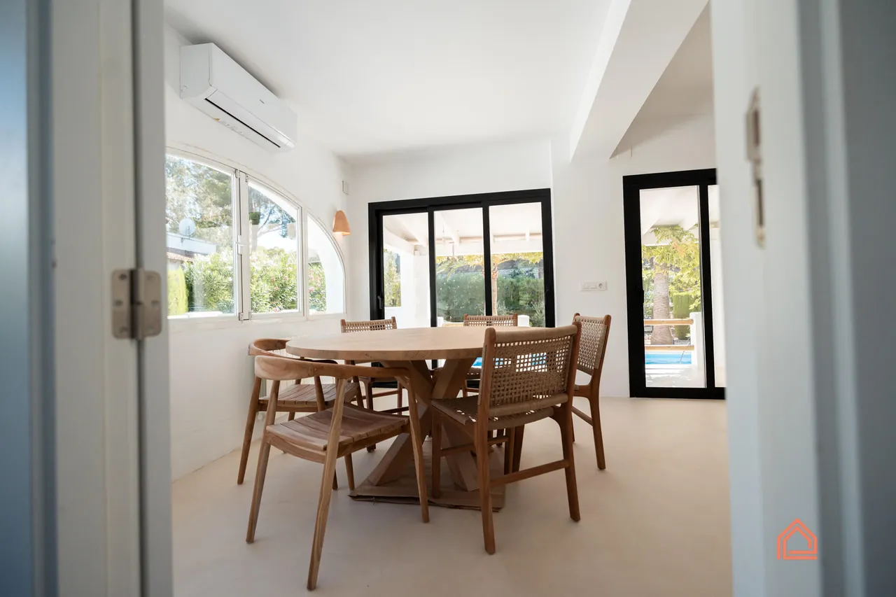 Dining area with round wooden table beside glazed doors to the pool