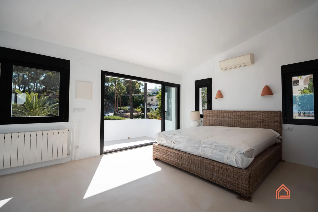 Master bedroom with rattan bed and garden views through large windows